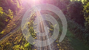 Railway at sunrise through green natural landscapes, the glow of sunlight in the camera lens