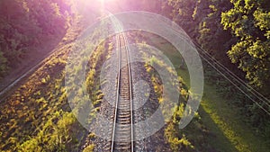 Railway at sunrise through green natural landscapes, the glow of sunlight in the camera lens