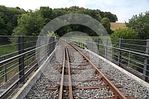 Railway track on a bridge surrounded by greenery under a cloudy sky