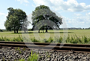 Railway track with meadows, trees and blue sky