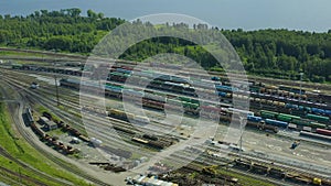 Railway tracks with freight trains, a locomotive with cars passing in the background. View from drone.