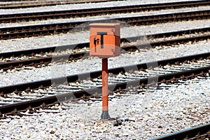 Railway trackside orange communication utility box mounted on metal pole and positioned on gravel between railway tracks