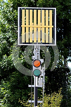 Railway trackside red and green traffic signal lights below signal sign mounted on metal pole at local train station