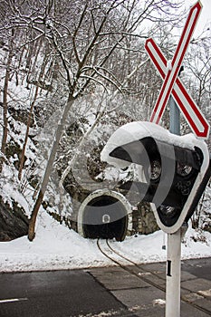 Railway tunnel in snowy forest with crossing sign and traffic lights foreground. Transport and railroad concept.