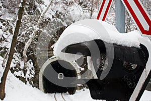 Railway tunnel in snowy forest with crossing sign and traffic lights foreground. Transport and railroad concept.