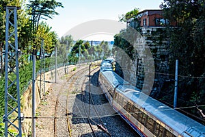 The railway turns towards the sea. Train on the railway with sea view. A train between the green trees and the stone