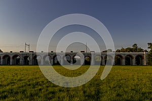 Railway viaduct with passing trains and cars in an underpass during a sunny day with moving clouds in the sky