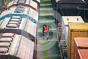 Railway worker in overalls with a hammer examines the old freight car.