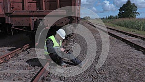 Railway worker with tablet sitting on rails near wagons