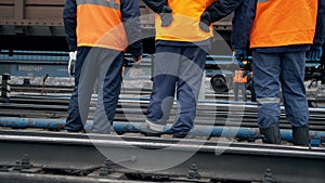 Railway workers are standing and looking at a passing train. Legs close-up. Worker in orange workwear