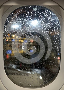 Rain, airport lights on plane window. Delay flight.