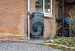 Rain barrel in front of a modern house, rainwater tank to collect rainwater and reuse it in the garden