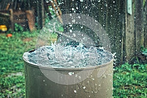 Rain barrel. Strong stream of water pours into an old metal barrel during heavy rain