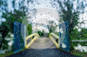 Rain droplets on the surface of car glass with blurred green nature and bridge background through window glass of car covered by r