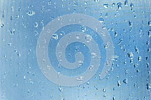 Rain drops on the blue glass bokeh background, shiny raindrops on a glass surface, water drops in a swimming pool closeup