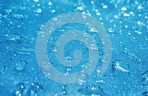 Rain drops on the blue glass bokeh background, shiny raindrops on a glass surface, water drops in a swimming pool closeup