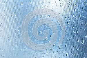 Rain drops on the blue glass bokeh background, shiny raindrops on a glass surface, water drops in a swimming pool closeup