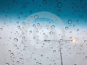 Rain drops on the car sunroof with lamp pole on the street backdrop