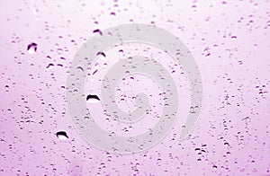 Rain drops on car window in purple tone with blur effect.