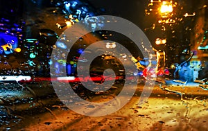 Rain drops on car window with road light bokeh, City life in night in rainy season abstract background,water drop on