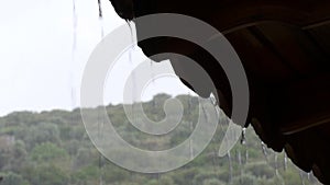 Rain drops falling from roof`s eave during rain