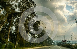 Rain drops on glass of the car, blurred trees and road background
