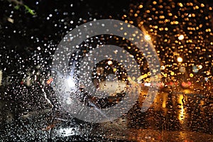 Rain drops on glass of car window with street bokeh at night in rainy season