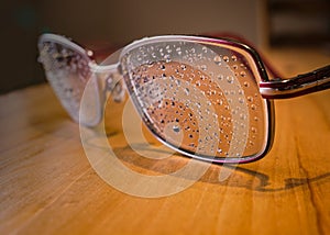 Rain drops on the lens of a pair of glasses on a wooden table, with slight lens flare