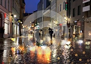 rain drops rainy street night people walking with umbrellas evening light reflection blurred on pavement Tallinn old town medieva