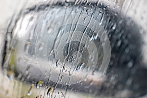 Rain drops rolling on window in storm, and a blurred black car side view mirror on a background, close up