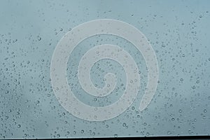 Rain drops sticking on the window pane in heavy downpour with cloudy sky on the background