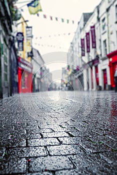 Rain drops on stone pavement in focus. Empty small street with shops of old town out of focus. Dark and muted colors, Autumn and