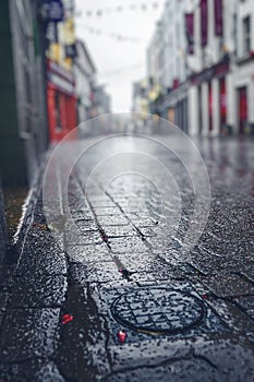 Rain drops on stone pavement in focus. Empty small street with shops of old town out of focus. Dark and muted colors, Autumn and