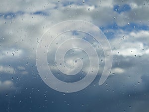 Rain drops on the window with clouds and sky background