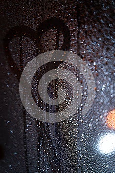 Rain drops on window with road light bokeh, heart symbol painted with drops