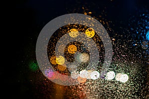 Rain drops on the windshield of car with colorful light bokeh in the evening during rainy season. Abstract of water droplets with