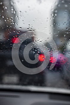 Rain drops on the windshield seeing from an interior of a car during a traffic jam.