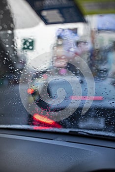 Rain drops on the windshield seeing from an interior of a car during a traffic jam.