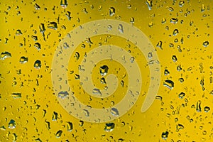 Rain drops on wndow glass on yellow background, close up shot