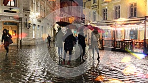 Rain evening rainy street people walk with umbreellas city blurred light wet pavement medieval houses in Tallinn old town