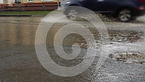 Rain falling on road, flowing through sewer drain. Cars drive on a flooded way.