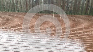 Rain falling on rust stained deck against wooden fence