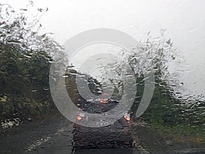 Rain falls on the windshield of a car. Raindrops from inside the vehicle. The taillights of a car seen through the windshield, on