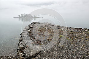 Rain and fog on the fjord, the pier and an small island in the mist, Norway