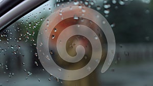 Rain on glass of car window with blurred woman raising umbrella in slow motion at background. Unrecognizable Caucasian