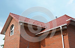 Rain gutter pipe system. Close up on attic brick house with clay roof tiles and plastic roof gutter pipes drain. Guttering