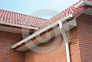 Rain gutter pipe system. Close up on Brick house with roof tiles and plastic roof gutter pipes drain. Guttering. Roofing
