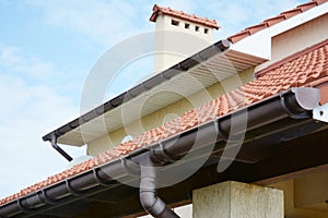 Rain gutters system on new house with chimney, red clay tiled roof and gable and valley type of roof construction