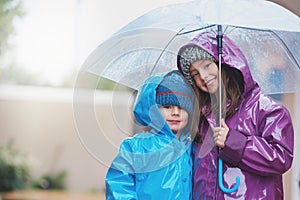 The rain never stopped us from having fun. Portrait of two siblings standing under an umbrella outside.