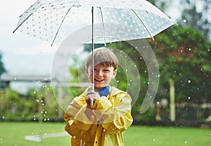 Rain never stops him from going outside. Portrait of a cheerful little boy standing with an umbrella outside on a rainy